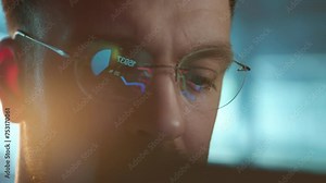 Trader wearing glasses is working on laptop computer. Screen with stock market charts and Bitcoin BTC or Ethereum ETH data analysis reflection. Broker trading online. Altcoins crypto currency trading
