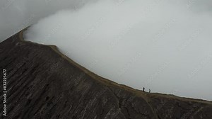 Two people walking on the Bromo volcano crater while it's smoking in Java, Indonesia, drone rotating around them