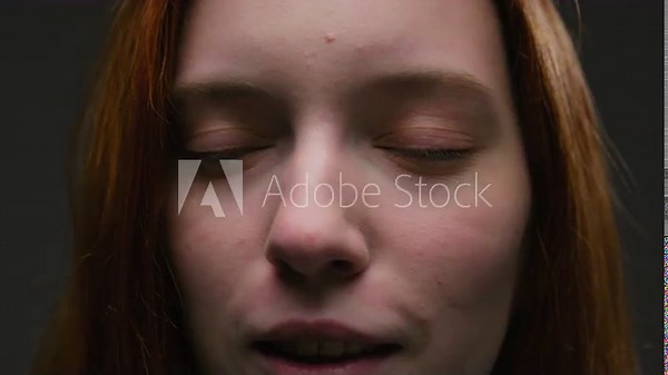 Portrait of a close-up beautiful red-haired girl, moves and shakes long red hair in slow motion. Attractive millennial woman in the studio, green eyes looking at the camera. Professional female model