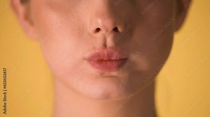 Extreme close up of woman lips making skeptical or superior gestures with her lip and puffing her cheeks against a yellow background in slow motion