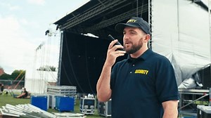 Security worker at outdoor stage for music festival or concert talking into radio - shot in slow motion
