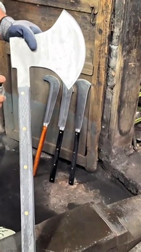 sharpening a large metal axe blade using a professional electric belt sander for a smooth finish