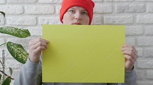 A man without emotion holds an empty yellow poster for typing in his hands, a young guy with a blank sheet in his hands for copy space