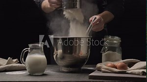 Professional baker sift flour through sieve in metallic bowl at black background. Sifting flour through sieve for baking. Bakery concept. Cook preparing dough at wooden table in 4K, UHD