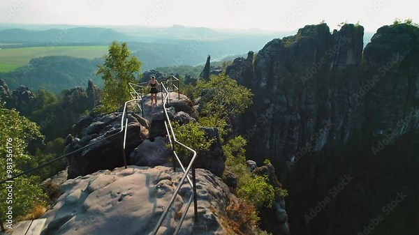 Woman hiking to the top of a scenic lookout point with wide views of green valleys and rock formations in Saxon Switzerland Germany Schrammsteine Elbe Sandstone Mountains