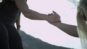 Person helping another person up a steep path giving a helping hand. Women achievement, success, empowerment and strength.