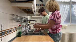 Mother and teenage son washing dishes together in the kitchen, sharing household chores in a relaxed and cooperative family moment