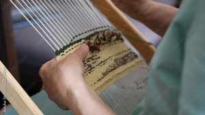 Woman creating small-format tapestry piece using hand loom and weft beater, selective focus. Pushing weft threads down with wooden tapestry beater