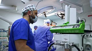 Attentive anesthesiologist looks at the medical equipment monitors. Focused medic controlling the patient's condition at operation. Low angle view.