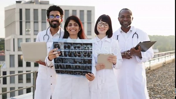 Group of multiethnic medical workers standing outdoors behind young indian colleague using laptop and looking together at results of patient's tests. Concept of technology, good treatment and medicine