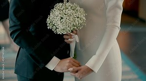 A bride and groom stand together and hold each other's hands. Beautiful slow motion video shoot of a bride and groom on a wedding day. Hand in hand next to each other.