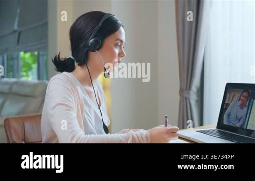 Young woman with headset woman participating in a video call, writing notes at a table in a well-lit indoor environment Stock Video Footage - Alamy