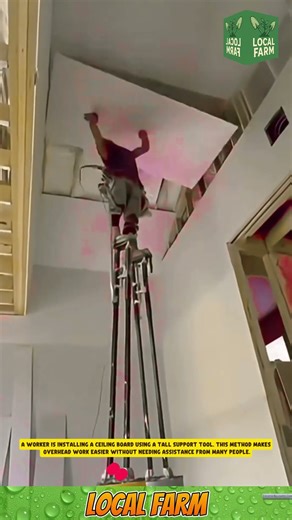 A worker is installing a ceiling board using a tall support tool.