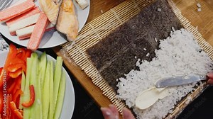 Making sushi on a makisu rolling mat with fresh ingredients on table