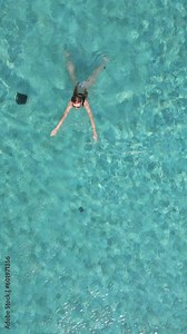 Top view of a young woman swimming in the pool in slow motion. Concepts of sunny pool relaxation, relaxing poolside retreat, tranquil aquatic escape, and leisure.