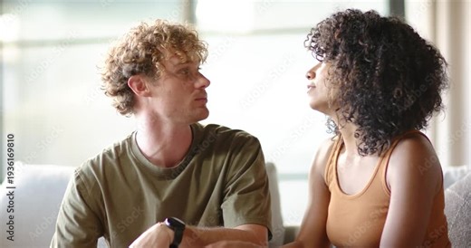 Couple sitting on sofa by window, woman initiating conversation, leaning in and sharing story
