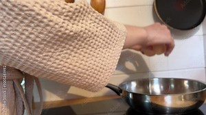 In a warm and cozy kitchen, a girl in a dressing gown skillfully prepares a nutritious meal - scrambled eggs, breaking eggs into a frying pan, demonstrating basic cooking techniques and fresh ingredie
