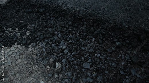 Slow motion video of the cross-section of a new road in Siska, Ljubljana, reveals the distinct layers of construction: a base of compacted grey aggregate and a thick, fresh layer of black asphalt.