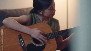 Asian female learning to play guitar at home while quarantined.