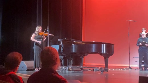 The college choir singing on stage risers with a red background ambience featuring a violinist. | Montgomery County Community College