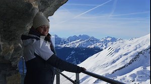 Woman enjoying scenic view of Swiss alps mountain view standing by cliffside in elevated metal handrail support during winter season