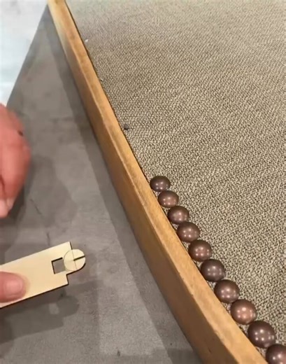 Installing nailhead trim by hand using a spacing guide to keep every tack perfectly aligned across the furnature edge.