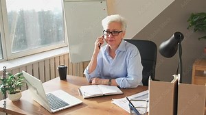 Confident middle aged senior woman talking on smartphone at workplace. Stylish older mature lady businesswoman making answering call by cellphone in office. Boss leader having conversation by mobile