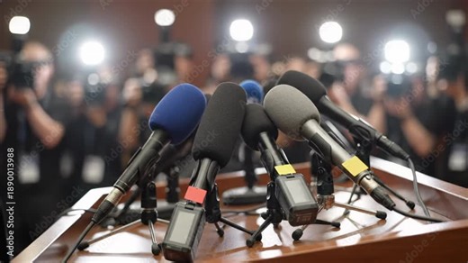 Cluster of News Microphones on Podium with Flashing Cameras in Press Briefing Room