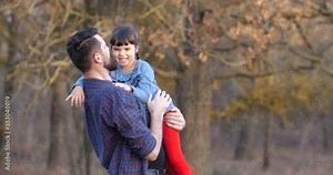 Father with daughter walking in beautiful autumn forest. Tall man with beard in plaid shirt holding in arms and hugging little girl, smiling and having fun. Father's day concept. 50 fps slow motion 4k