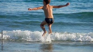 Little boy jumping on the waves at the line of the sea surf.