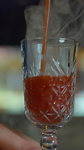 Close up of bartender at a bar counter pouring alcohol into vintage glass. Media. Pouring red hot alcoholic tincture with steam.