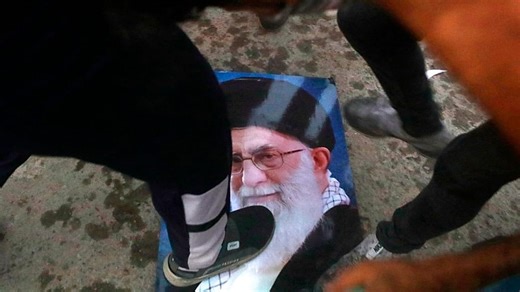 Iranian women light cigarettes on burning portrait of the ayatollah
