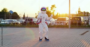 Funny spaceman in the full costume and armor dancing and moving at the parking on the sunset sunlight outside. Astronaut being happy to come back on Earth. Stock Video