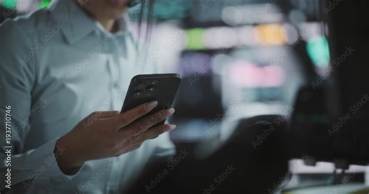 Trader Multitasking at Workstation, Typing Urgent Message on Smartphone, Keeping Close Eye on Fluctuating Financial Graphs. Instant Communication, Continuous Market Tracking in Modern Stock Exchange.