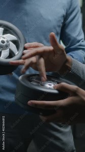 Two diverse automotive male designers holding small wheels, developing futuristic electric car design, standing near whiteboard with blueprints. They working in car design development modern studio