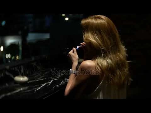 A beautiful elegant lady sits alone in a nightclub on the terrace smoking a cigarette. 4k,