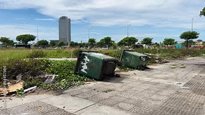 A photograph capturing a fallen dumpster and scattered garbage against a grassy field, with a backdrop of blue sky and clouds. This image highlights environmental pollution and waste management issues