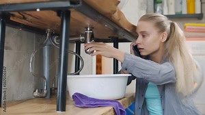 Woman sitting near leaking sink in laundry room calling for help