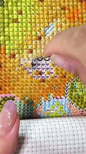 Stitching a colorful cross stitch pattern with a needle and yellow thread on white aida fabric