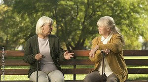Two senior ladies arguing and sitting on bench in park, grumpy elders, dispute