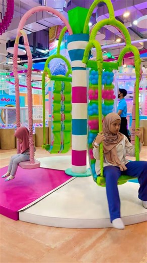 The older sister rides the green swing and the younger sister rides the pink swing that spins.