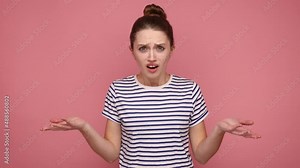 Irritated indignant woman, raising hands in anger and shouting why how, what do you want, quarreling, looking at camera, wearing striped T-shirt. Indoor studio shot isolated on pink background.