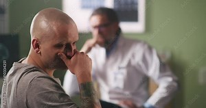 Bald man reacting to band news and talking with oncologist