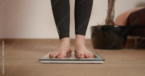 Young woman stepping on scale and wiggling her toes while checking her weight after workout and fitness