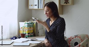 Smiling beautiful woman dictating voice answer, communicating with friends in social network, using smartphone application at home, recording audio message or activating ai virtual assistance.