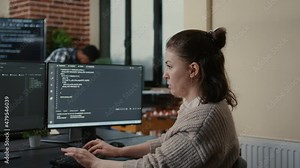 Portrait of focused software engineer writing code looking at multiple computer screens displaying programming language algorithm. Programer coding while colleagues doing teamwork app developing.