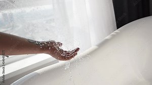 Beautiful woman enjoying jets of hot water in the palm of her hand in a luxurious bathroom with a window. Lifestyle and beauty care concept.