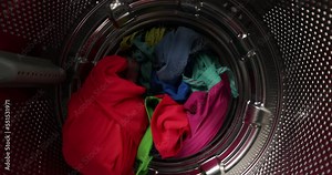 View from inside a washing machine, a man puts a colored wash into the washing machine