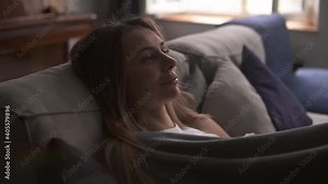 Smiling beautiful woman sitting in room on the sofa dreaming of something good, wrapped with plaid