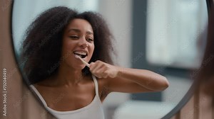 Reflection in mirror African American woman holding toothbrush brushing white teeth biracial girl female cleaning mouth oral hygiene procedure morning dental care routine whitening tooth with brush